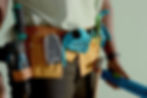 Close-up of a person wearing a yellow tool belt with screwdriver, drill, and measuring tape, holding a blue level. Greenish background.