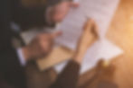 Two people review a legal document at a wooden table; one points while the other holds a pen. A judge’s gavel and sunlight visible.
